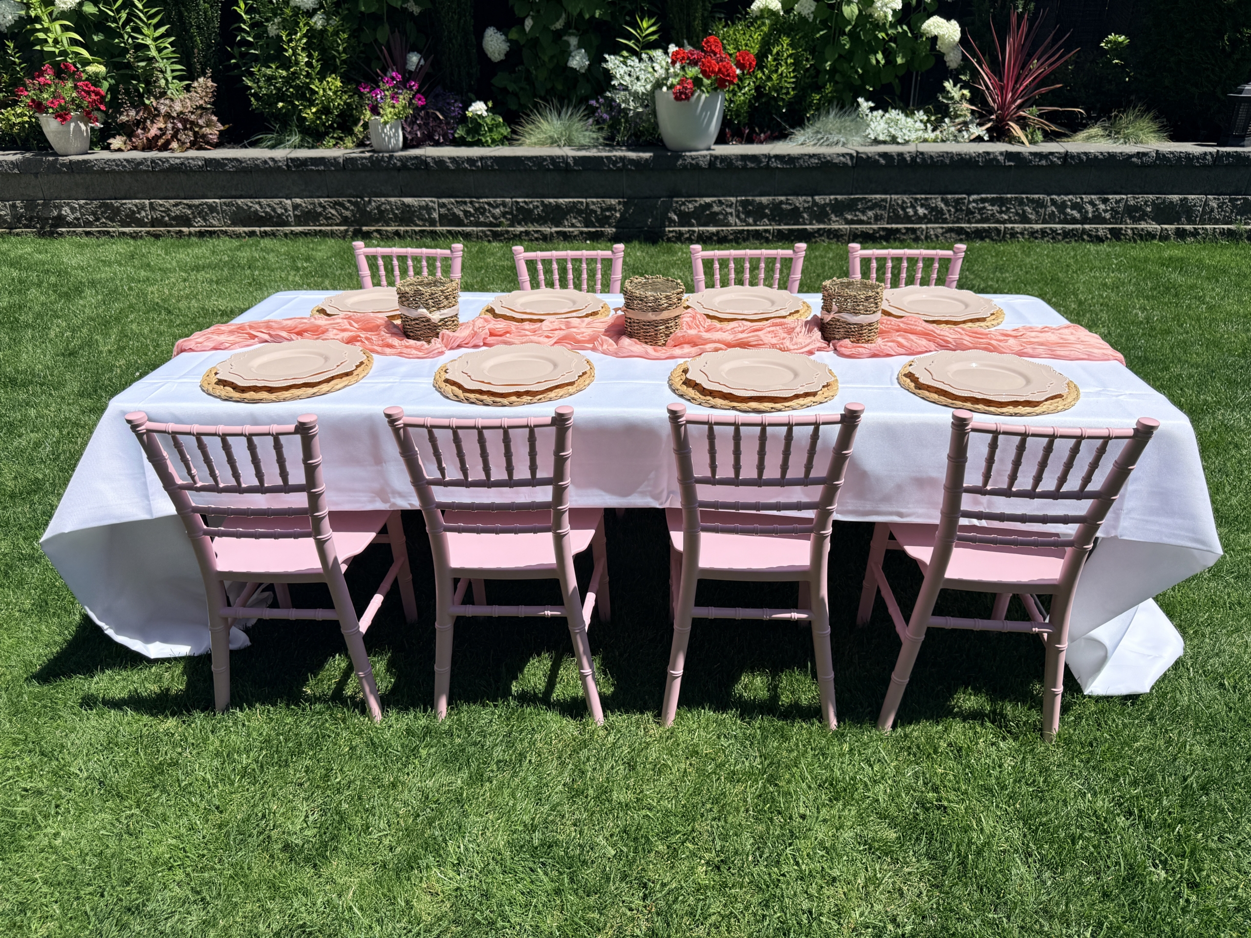 Fully styled pink kids tablescape with chiavari chairs and blush place settings in a garden backyard